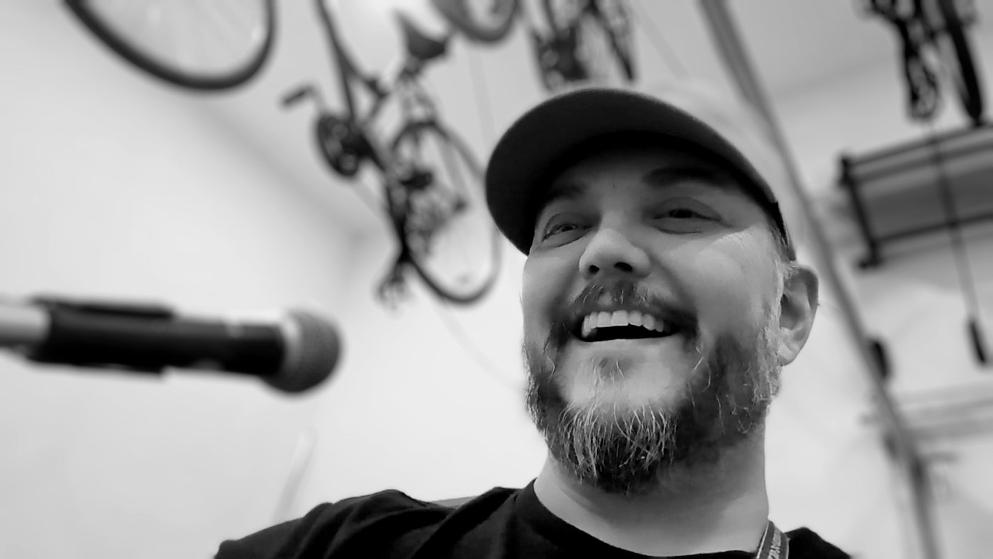 Black and white photograph of Jeremy singing into a microphone, lit dramatically with bikes in the background