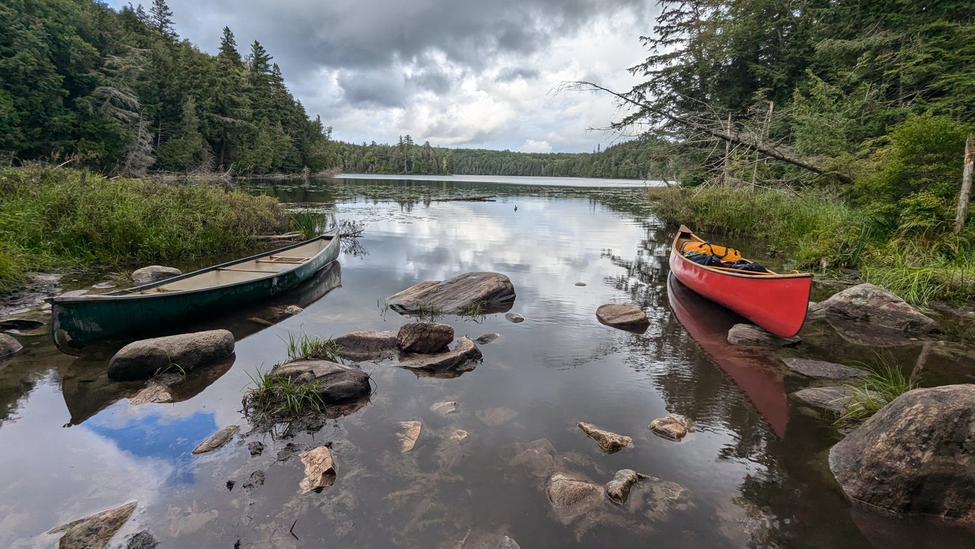 Photograph of two canoes on a still lake surrounded by forest — green canoe on left, red canoe on right